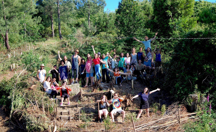 Estudiantes erasmus arrancan acacias para plantar árboles autóctonas y frutales en un bosque gallego