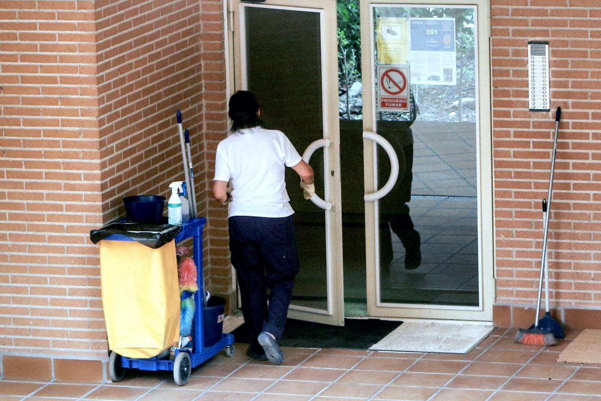 Una trabajadora de la limpieza entra en un edificio con el carrito de la limpieza.