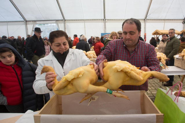 Dos personas sujetan un capón en la tradicional Feria de Navidad, `Feira do capón de Vilalba´. donde se venden los mejores capones para la cena de Nochebuena de toda España, en Lugo-Galicia (España), a 22 de diciembre de 2019.