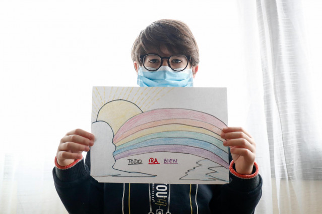Un niño con mascarilla enseña un dibujo que ha hecho de un arcoiris y la frase 'Todo irá bien' cuando queda tan solo una semana para que niños y preadolescentes puedan salir a la calle durante el confinamiento por el coronavirus
