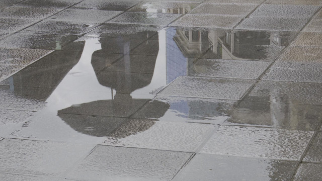 Una persona con paraguas se refleja en un charco provocado por la lluvia esta mañana en Bilbao.