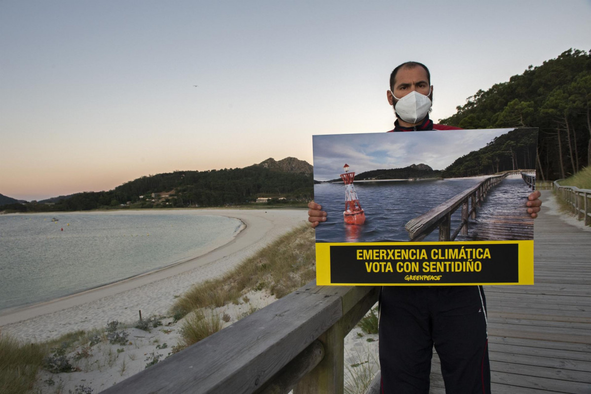 Un voluntario de Greenpeace porta una fotografía modificada de la Praia de Rodas, en las Illas Cíes, para simular los efectos de la subida del nivel del mar.