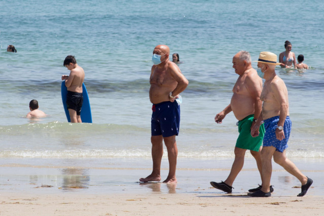 Tres hombres protegidos con mascarillas pasean por la Playa de A Rapadoira en Foz