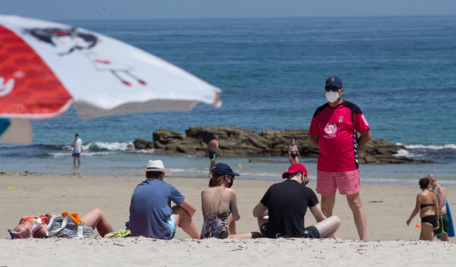 Varias personas protegidas con mascarillas toman el sol en la Playa de A Rapadoira en Foz, en la comarca de A Mariña.