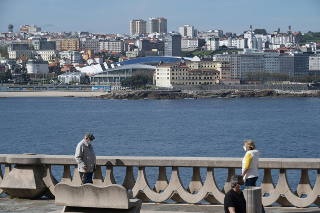 Dos personas pasean por el paseo marítimo de A Coruña (Galicia), con el estadio de Riazor de fondo, en el segundo día en que el Gobierno permite salir a hacer deporte de forma individual y pasear con otra persona con la que se conviva, a determinadas hora
