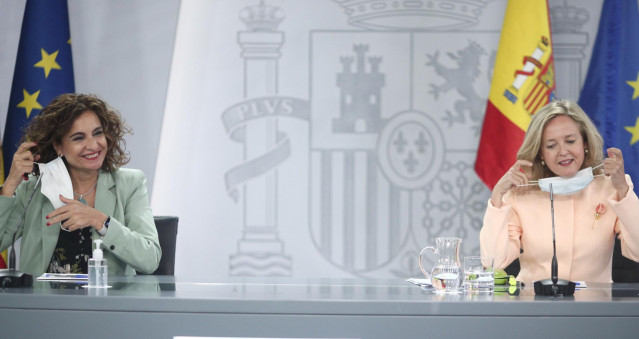 La ministra portavoz y de Hacienda, María Jesús Montero (i), y la vicepresidenta y ministra de Asuntos Económicos y para la Digitalización, Nadia Calviño, se quitan las mascarilla antes de comenzar la rueda de prensa posterior al Consejo de Ministros en M