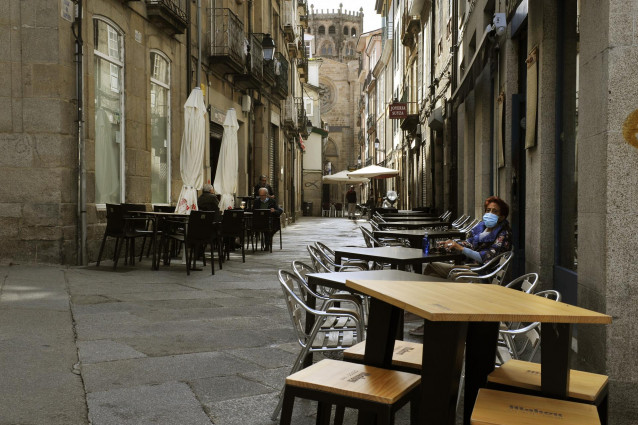 Una mujer permanece sentada en una terraza del barrio de O Couto el mismo día en el que han prohibido las reuniones entre no convivientes ante el aumento de contagios de Covid-19.