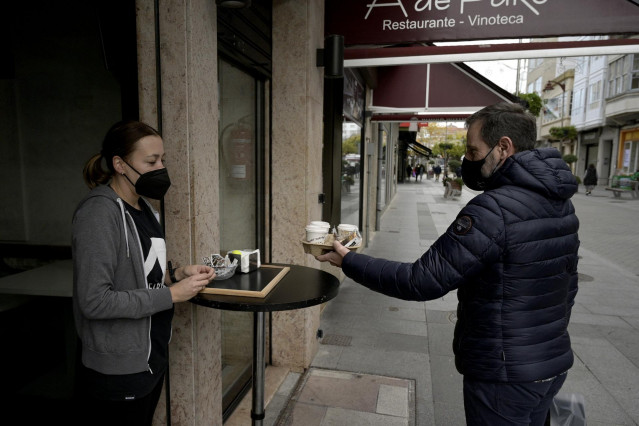 Un hombre recoge unos cafés de un establecimiento con las nuevas restricciones para la hostelería