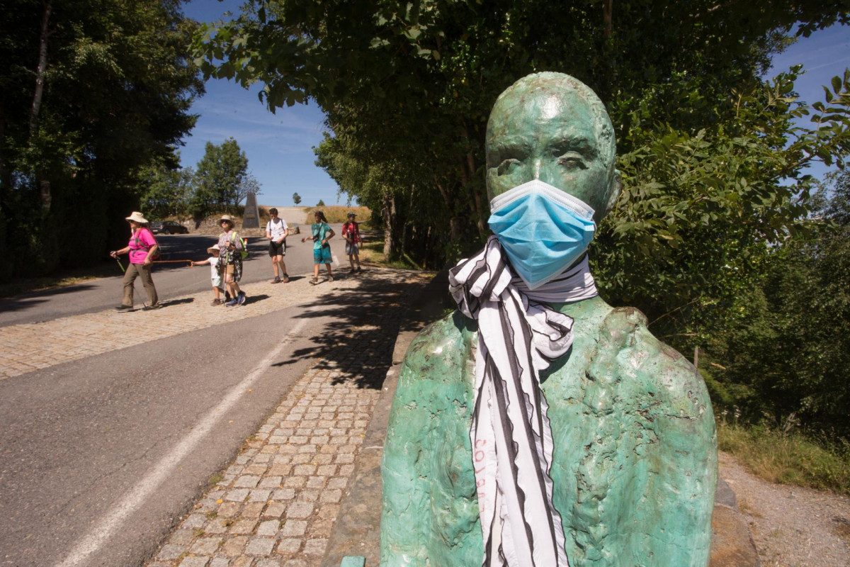 Un grupo de peregrinos llega a O Cebreiro pasando junto a la escultura del coruñés Miguel Couto, que luce desde hace semanas una mascarilla quirúrgica en recuerdo de las víctimas del Covid-19, mie