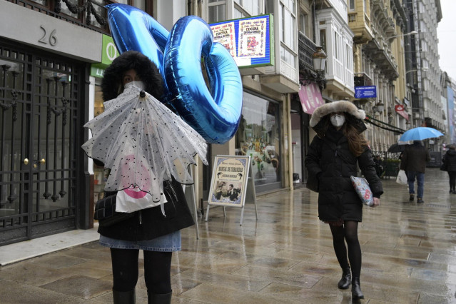 Transeúntes caminan protegidos por una vía de A Coruña