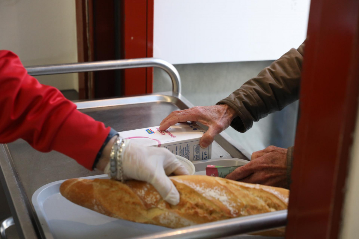 Un voluntario (i) trae comida a una persona (d) como parte del reparto diario de alimentos del Comedor Social San José, en Puente de Vallecas, Madrid (España), a 5 de febrero de 2021.