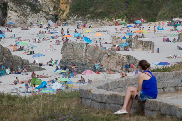 Archivo - Una persona sentada frente a la playa en A Mariña en julio de 2020.