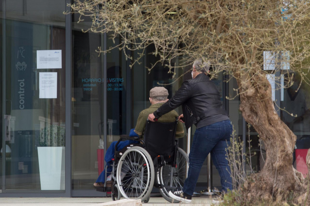 Una mujer pasea junto a un anciano en silla de ruedas hacia la residencia Albertia, a 17 de abril de 2021, en Lugo, Galicia (España). Una de las nuevas medidas incluidas en la desescalada de Galicia consiste en la ampliación de las posibilidades de visita