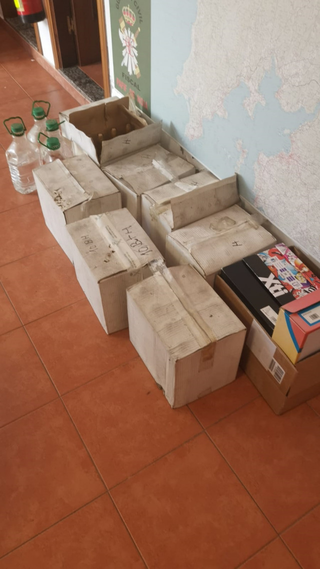 Cajas con botellas y garrafas de aguardiente y 60 cajetillas de tabaco sin precintas fiscales intervenidas en un almacén en Noia (A Coruña).