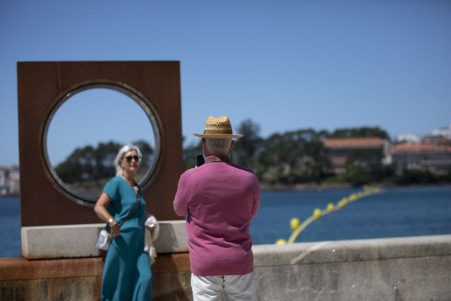 Un hombre echa una foto a una mujer en el paseo marítimo de la playa de Sanxenxo