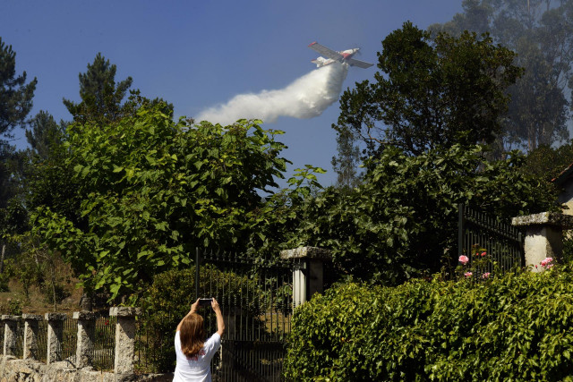La propietaria de una finca afectada por un incendio forestal fotografía con su teléfono móvil cómo un hidroavión arroja agua sobre el fuego, a 28 de julio de 2021, en la parroquia de Santa Mariña do Monte, Ourense, Galicia (España). Un total de seis avio