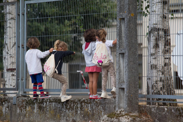 Varios niños y niñas se encaraman a la valla de un centro en el primer día de curso en Galicia.