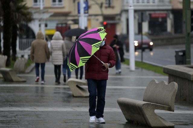 Un hombre con un paraguas camina por el paseo marítimo mientras llueve en A Coruña