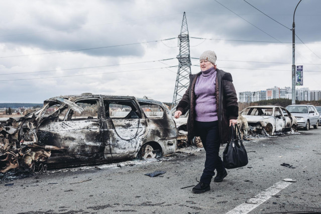 Una mujer camina delante de unos coches quemados en un puente de Irpin, a 7 de marzo de 2022, en Irpin (Ucrania). El ejército de Ucrania resiste por el momento el duro asedio de Rusia en algunas de sus ciudades, como Irpin y Kiev, donde se recrudecen los