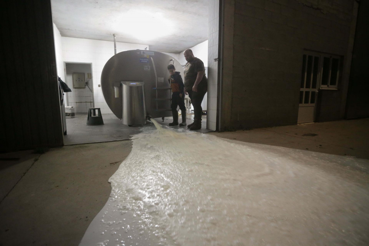 Un ganadero y un niño vierten la leche al suelo después de que la industria láctea tenga que parar su actividad a partir de hoy, a 17 de marzo de 2022, en Vilela, Outeiro de Rei, Lugo, Galicia (Esp