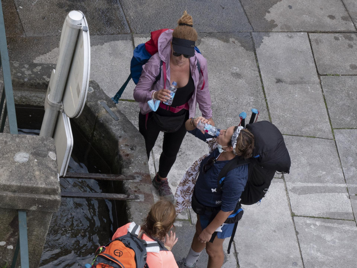 Archivo - Tres peregrinas beben agua en una fuente en Santiago de Compostela.