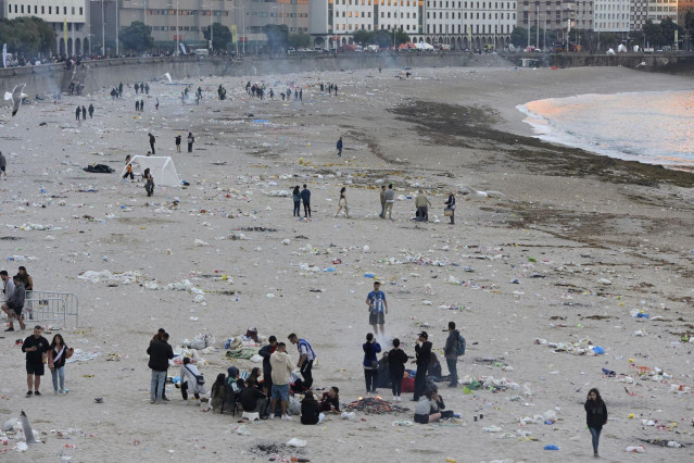 Vista general de la playa de Orzán con grupos de personas y restos de basura después de la celebración de las hogueras de la noche de San Juan.