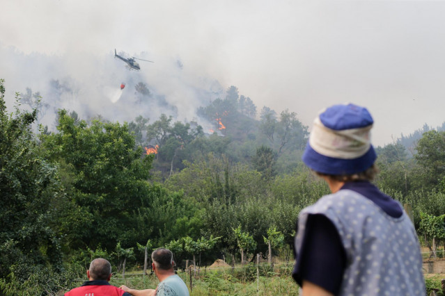 Varias personas observan cómo un helicóptero trata de extinguir un fuego en las inmediaciones de un incendio en Quiroga. Foto de archivo.