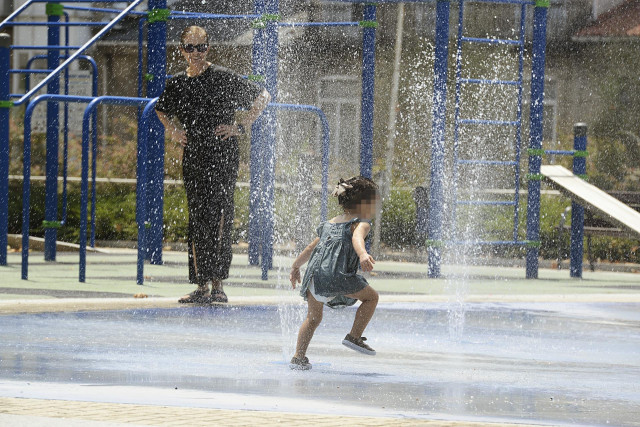 Dos personas se refrescan en unos chorros durante un día de la segunda ola de calor de verano en España, a 14 de julio de 2022, en Ourense,