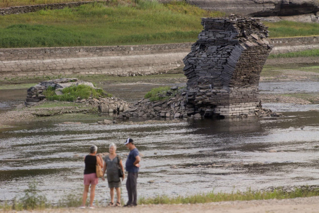 Tres personas junto al río Miño, cuyo bajo caudal ha dejado a la vista las ruinas del antiguo Portomarín, que en los años 60 del siglo pasado fue anegado por el embalse de Belesar, en Escairón, a 9 de agosto de 2022, en Escairón, Lugo, Galicia (España). L