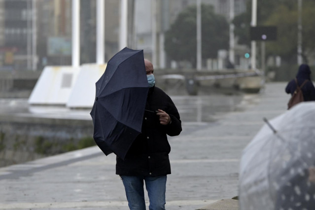 Archivo - Un hombre con un paraguas camina por el paseo marítimo mientras llueve, a 8 de diciembre de 2021, en A Coruña, Galicia, (España). La borrasca Barra ha hecho que la Xunta haya activado para todo el litoral gallego una alerta naranja por temporal