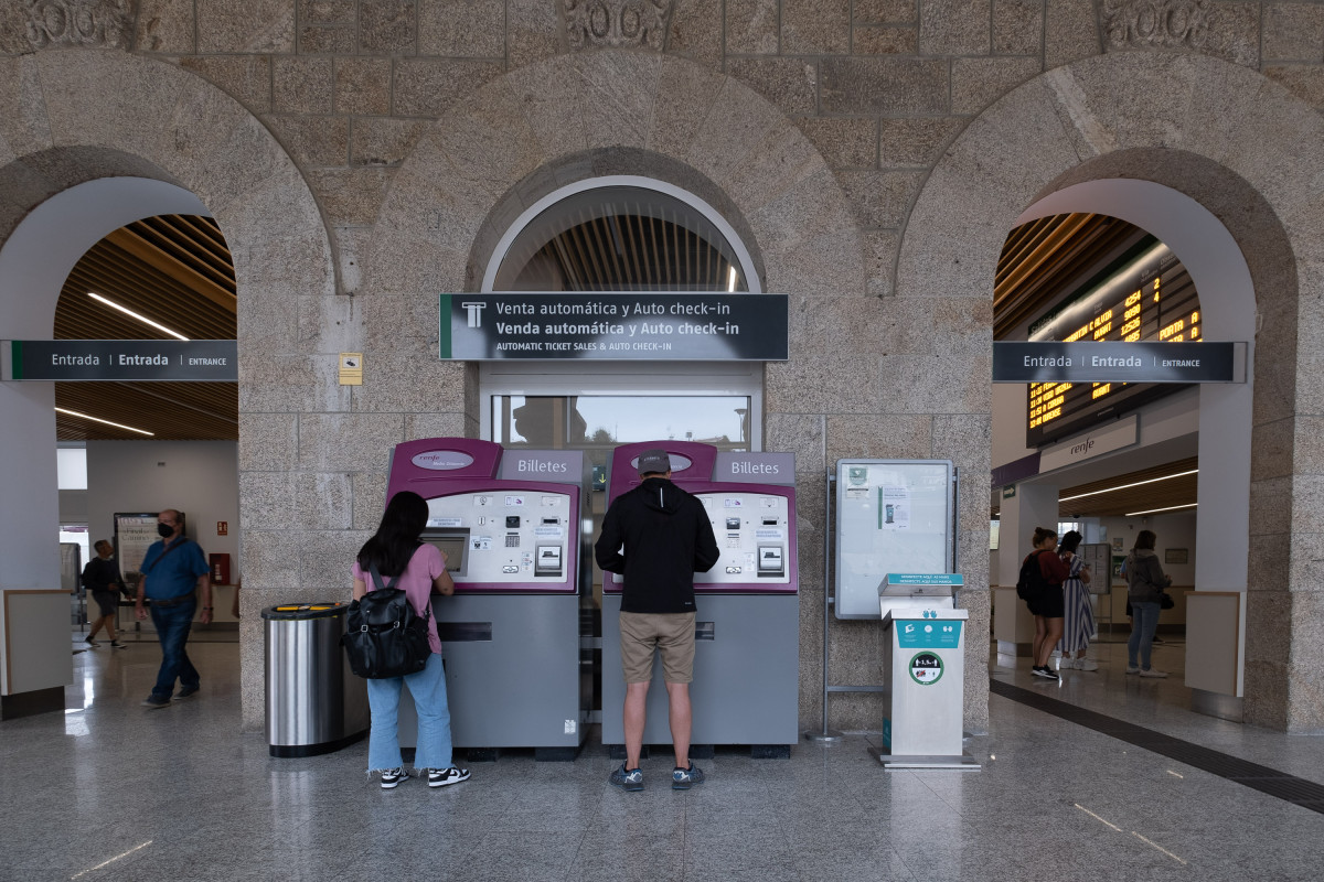 Dos personas compran billetes en los cajeros de venta automática en la estación de trenes, a 24  de agosto de 2022, en Santiago de Compostela, A Coruña, Galicia, (España). Los usuarios de Renfe en