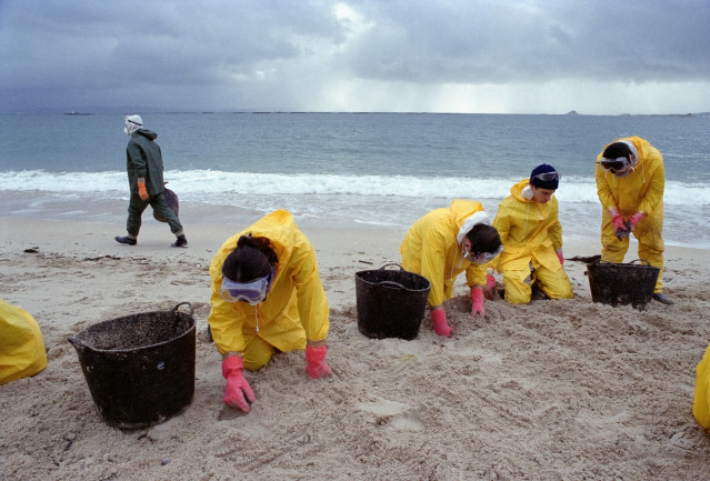 Archivo - Voluntarios limpian la arena de restos de fuel en la playa de Aviño, en el municipio gallego de Malpica de Bergantiños, tras el Prestige