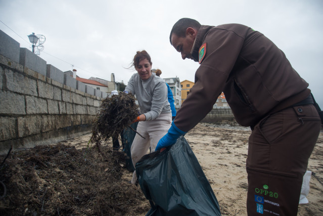 Una voluntaria y un agente rural de la zona recogen los restos de chapapote mezclados con algas, a 13 de diciembre de 2022, en Illa de Arousa, Pontevedra, Galicia (España). Por el momento se desconoce el origen del vertido de chapapote, pero fuentes munic