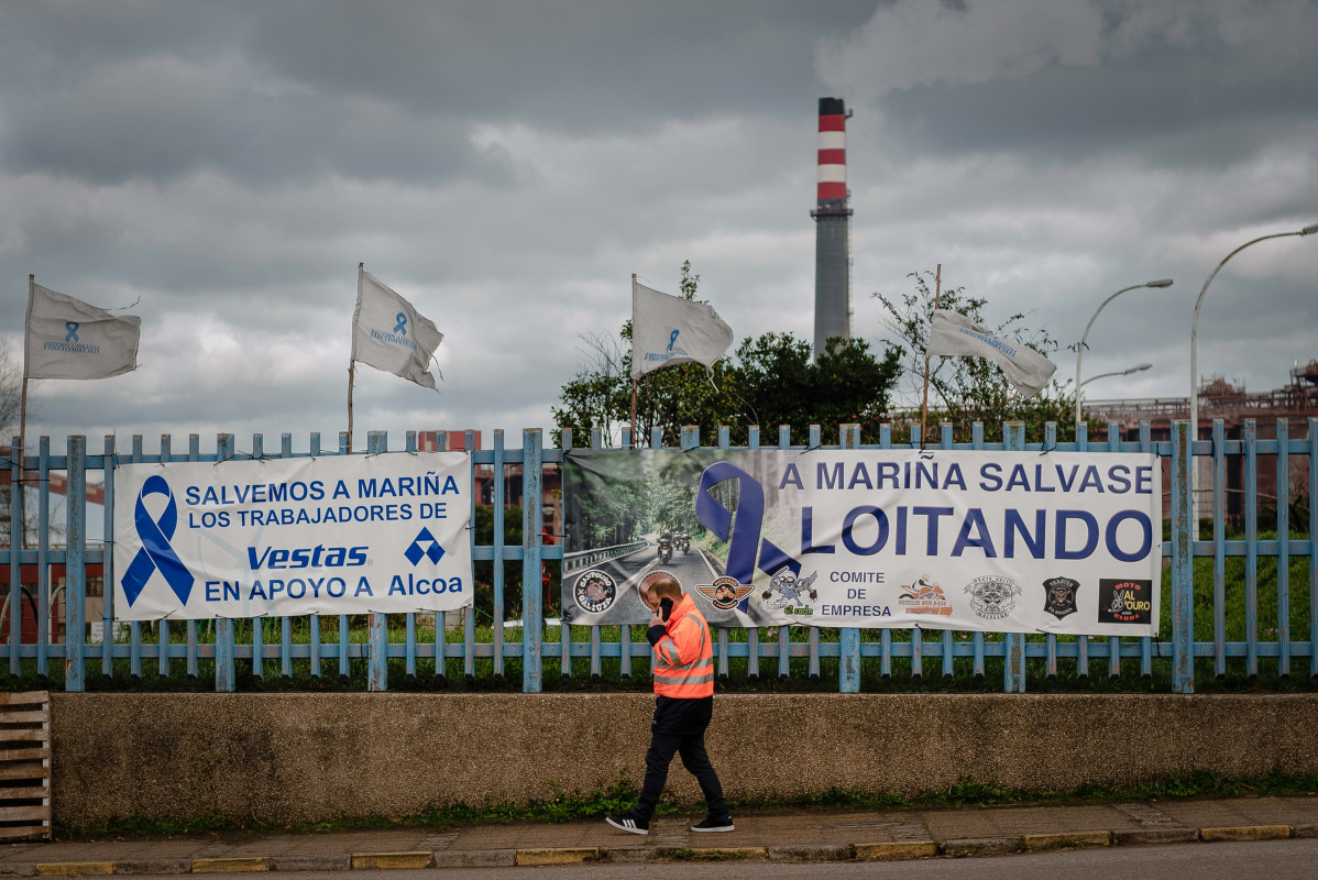 Archivo - Una persona pasa delante de una pancarta, colocada por los trabajadores en la valla de la fábrica de Alcoa en San Cibrao, un día después de que los trabajadores alcanzaran un acuerdo con 