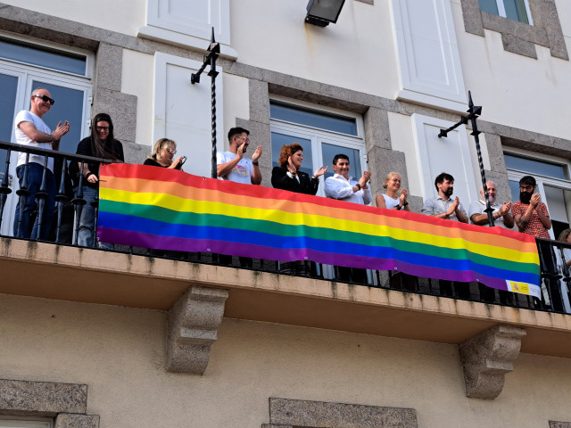 Representantes del colectivo han desplegado una bandera conmemorativa en la fachada de la Delegación del Gobierno en Galicia, acompañados por el delegado, Pedro Blanco, y la subdelegada en A Coruña, María Rivas