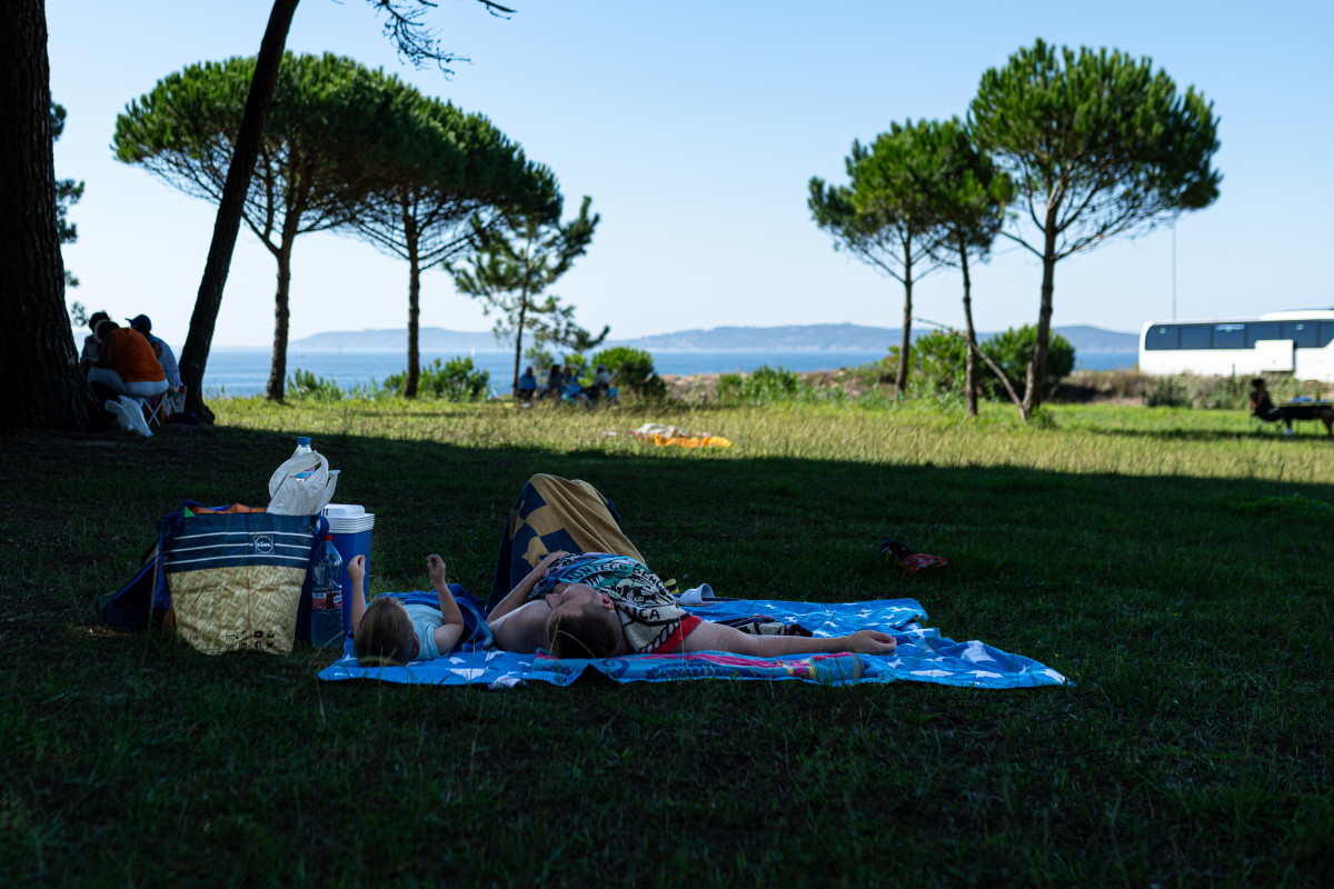 Un hombre y un niño descansan a la sombra de un árbol, a 30 de septiembre de 2023, en Sanxenxo, Pontevedra, Galicia.