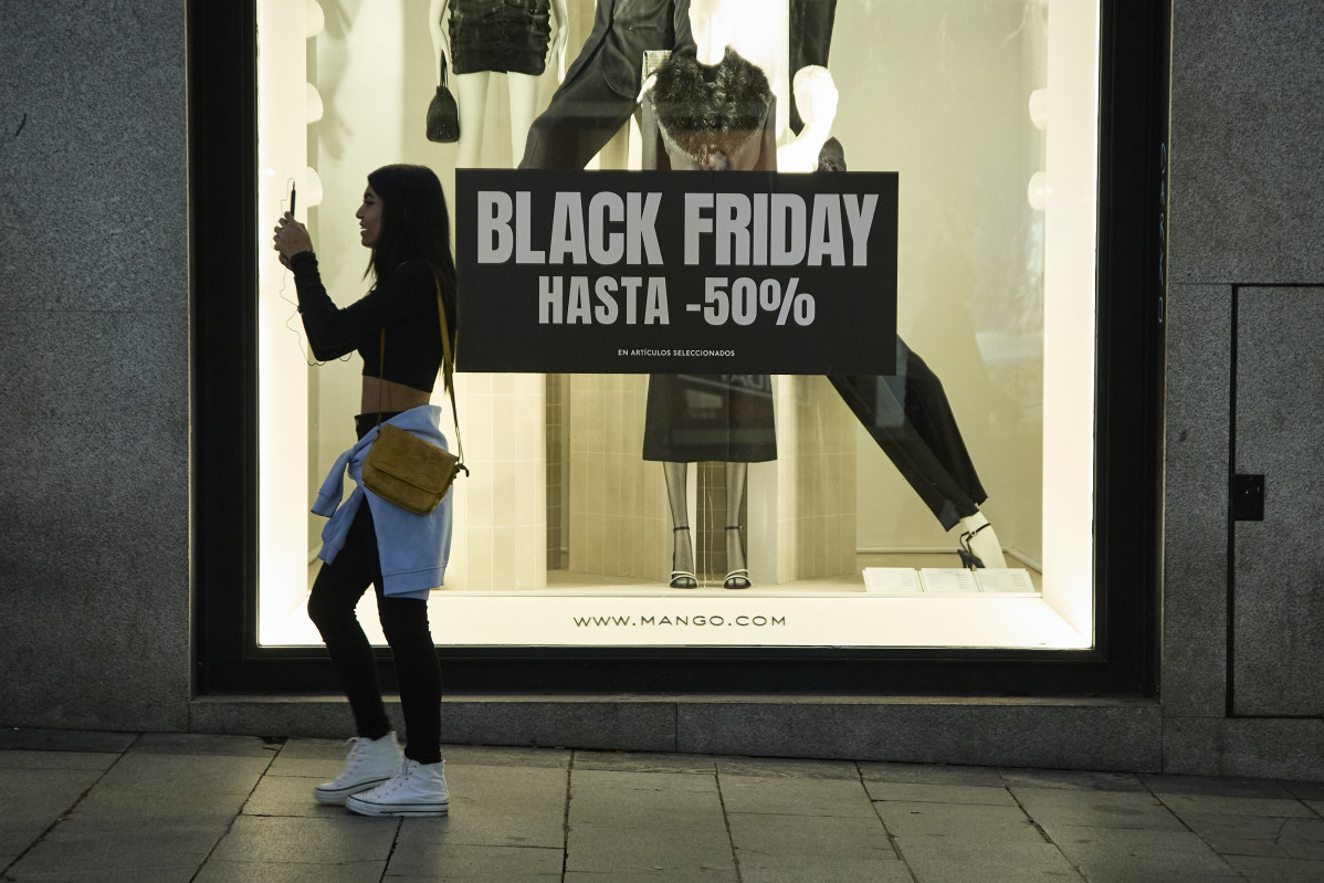 Archivo - Varias personas pasan por delante de los comercios que anuncian los descuentos del Black Friday