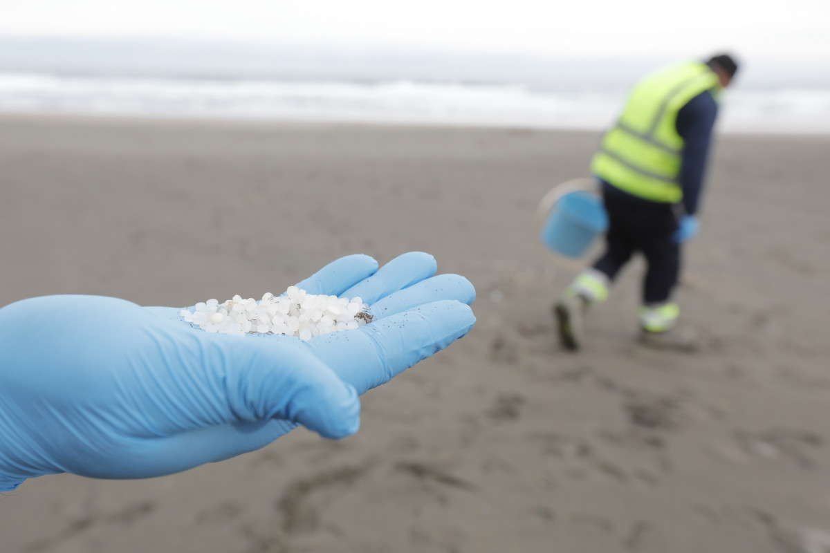 Archivo - Un operario de TRAGSA coge con la mano pellets de plástico, en la playa Otur, a 9 de enero de 2024, en Valdés, Asturias (España). El Principado de Asturias ha activado el nivel dos de eme