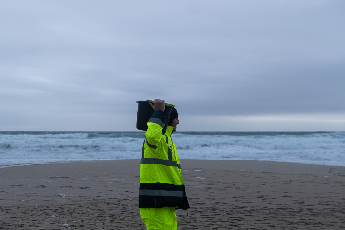 Un hombre carga un cubo lleno de pellets, en la playa Do Dique, a 13 de enero de 2024, en Queiruga, A Coruña, Galicia (España). La conocida ya como la “marea blanca”, se prevé que proceda de lo