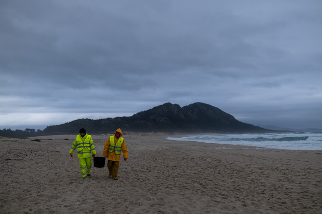 Dos hombres cargan un cubo lleno de pellets, en la playa Area Maior, a 13 de enero de 2024, en Muros, A Coruña, Galicia (España). La conocida ya como la “marea blanca”, se prevé que proceda de los seis contenedores del buque Toconao que cayeron al mar en