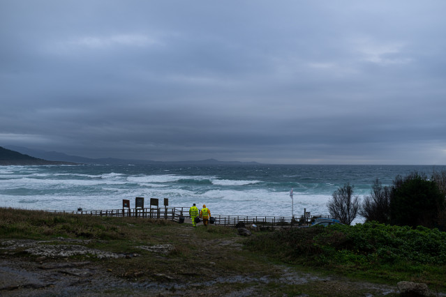 Dos hombres cargan un cubo lleno de pellets, en la playa Area Maior, a 13 de enero de 2024, en Muros, A Coruña, Galicia.