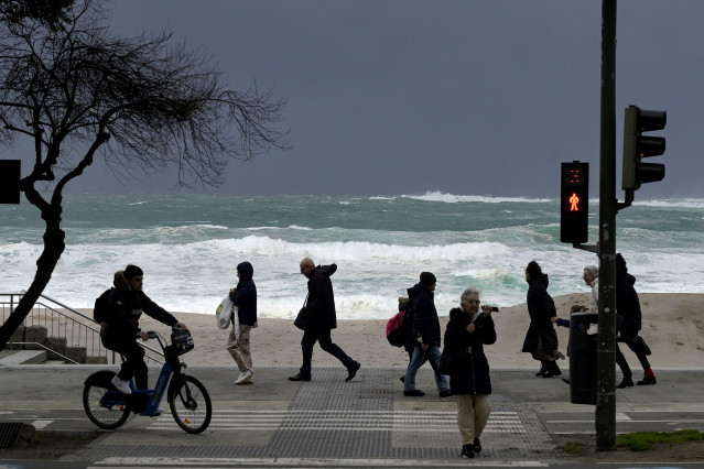 Archivo - Varias personas caminan delante de las olas durante un frente meteorológico, a 23 de febrero de 2024, en A Coruña, Galicia (España).