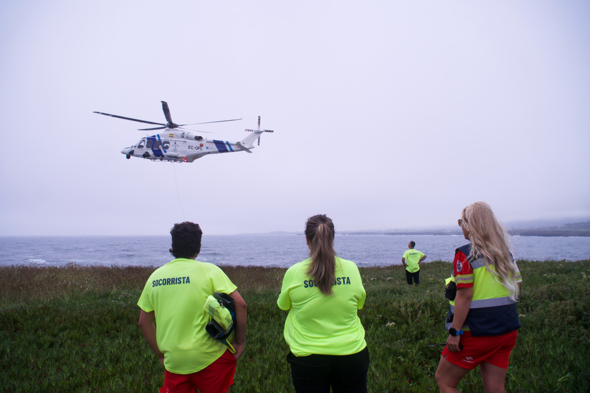 Varios socorristas observan a un helicóptero rescatando a un varón joven en la Punta do Castro, a 28 de julio de 2024, en San Pedro de Benquerencia, Barreiros, Lugo, Galicia.