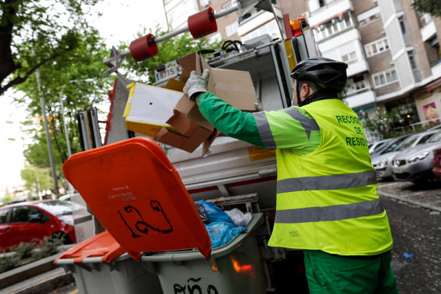 Archivo - Un operario de recogida de residuos protegidos con mascarilla extrae cajas de cartón de un cubo de basura para triturarlas en un camión de basura durante su trabajo de limpieza en una calle de la capital durante el día 33 del estado de alarma, e