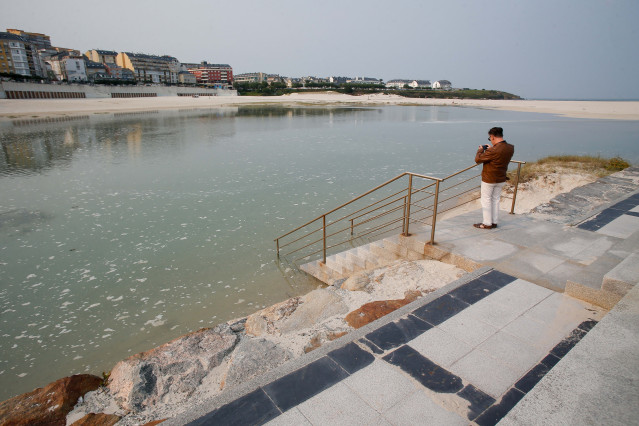 Archivo - Una persona fotografía la pleamar en el espigón de Foz, junto a la playa de A Rapadoira.