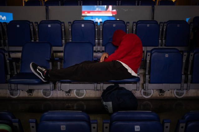Un hombre duerme en las gradas del estadio Movistar Arena.