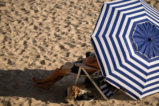 Archivo - Una persona descansa en la playa bajo la sombrilla.