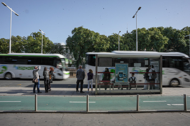 Archivo - Varias personas esperan en una parada de autobús