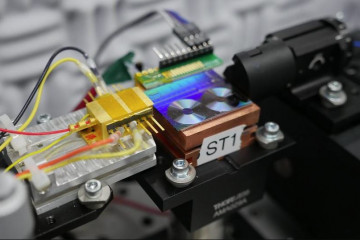 Archivo - Investigadores del NIST prueban un chip para convertir la luz en señales de microondas. En la foto aparece el chip, que es el panel fluorescente que parece dos pequeños discos de vinilo. L