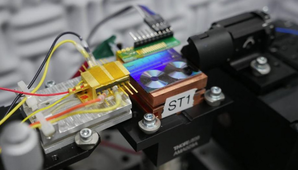 Archivo - Investigadores del NIST prueban un chip para convertir la luz en señales de microondas. En la foto aparece el chip, que es el panel fluorescente que parece dos pequeños discos de vinilo. L